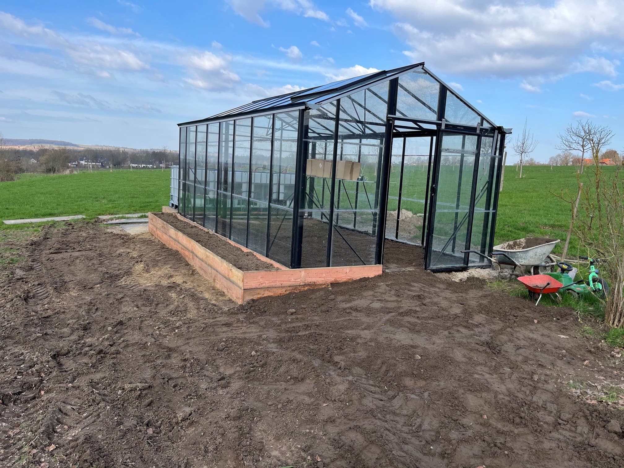 De glazen kas op Hoeve 1700 met zwart gecoate profielen, opgebouwd uit hergebruikt kasmateriaal, in glooiend heuvelland